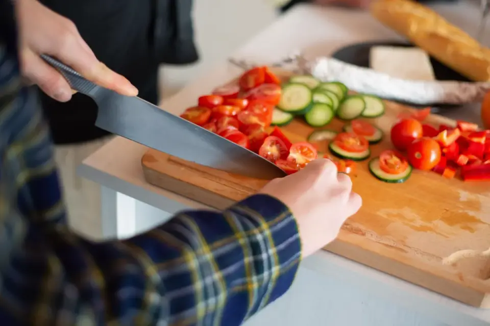 A dog looking up at its owner beside a kitchen cutting board with vegetables