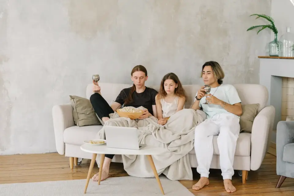 A family on a couch watching a movie with a dog nearby and a popcorn bowl on the table