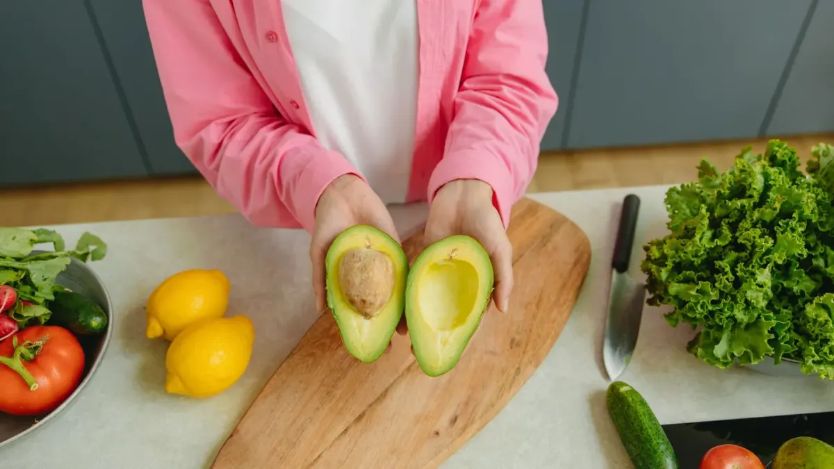 A halved avocado on a cutting board while a dog watches from the edge of the counter