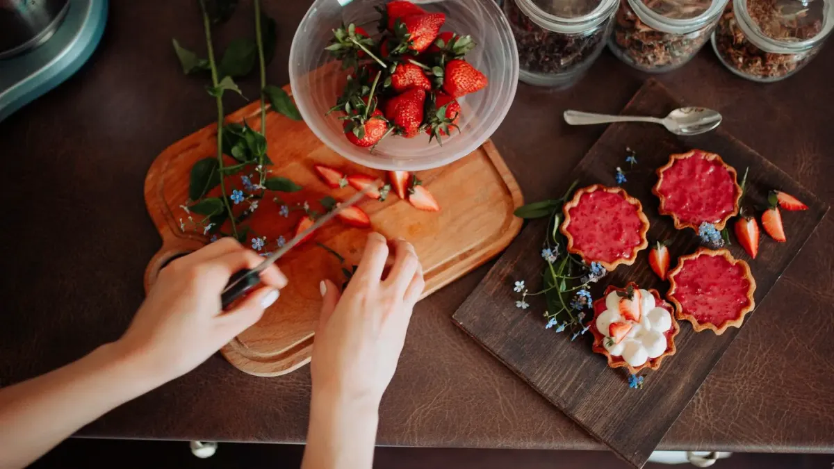 A small dog sniffing a bowl of sliced fresh strawberries on a kitchen counter