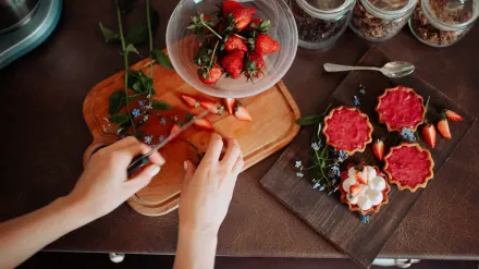 A small dog sniffing a bowl of sliced fresh strawberries on a kitchen counter