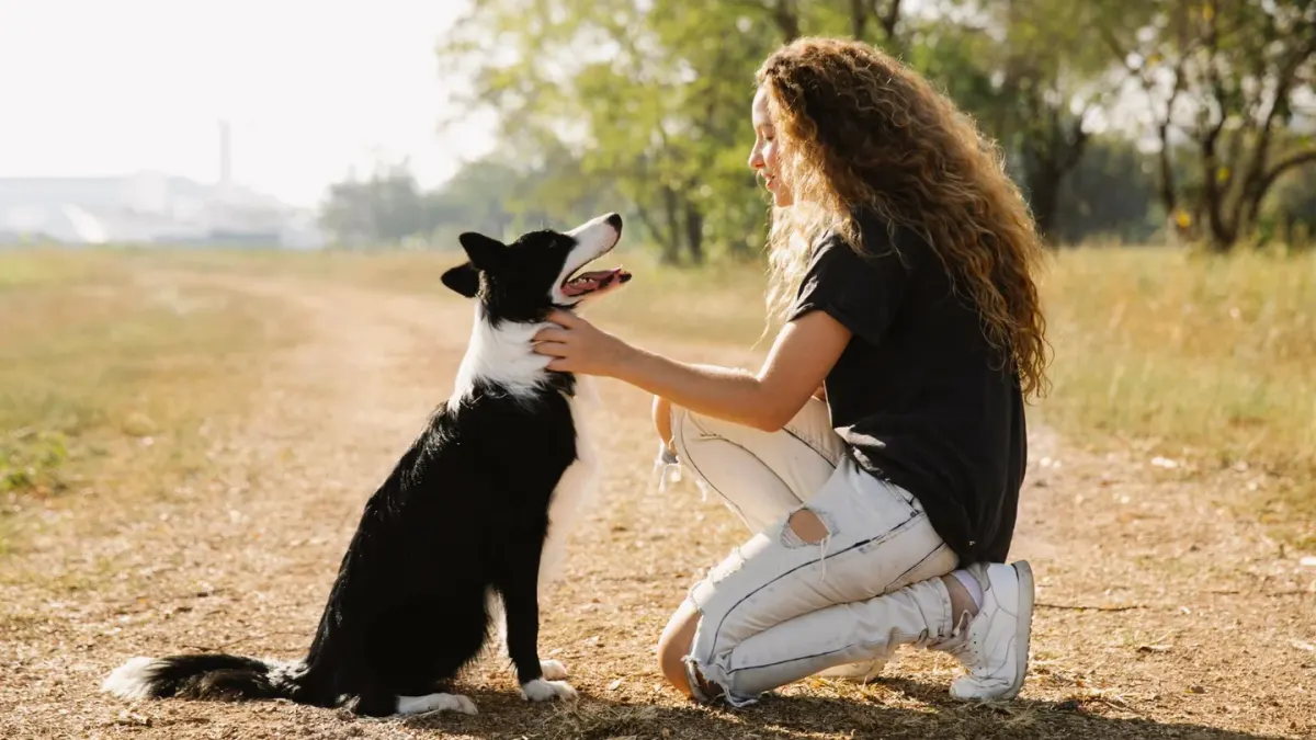 A woman kneeling beside a hesitant dog on a leash outside a clinic entrance