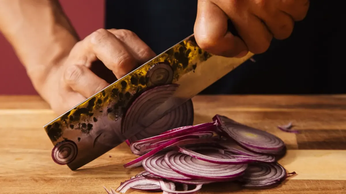 Chopped onions on a cutting board with a dog watching from a few feet away in a kitchen