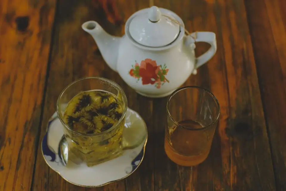 Dried chamomile flowers next to a piece of fresh ginger root on a wooden table