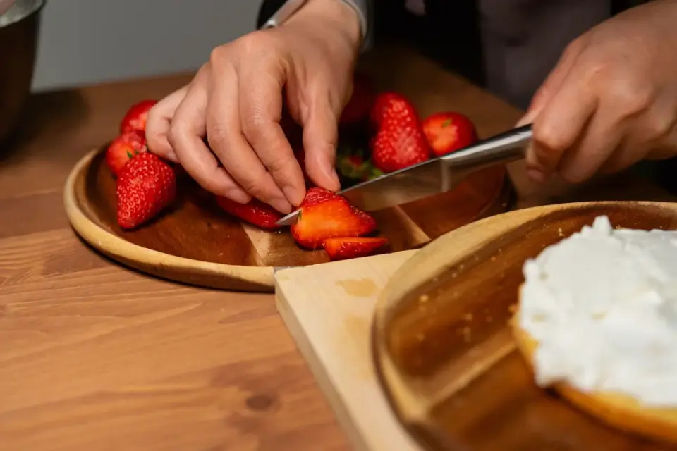 Hands slicing a fresh strawberry into small pieces on a cutting board